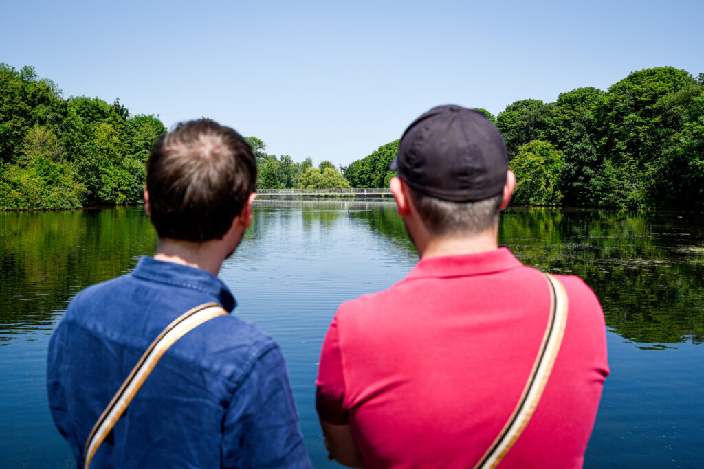 Zwei junge Männer stehen am Wasser und schauen in die Ferne.