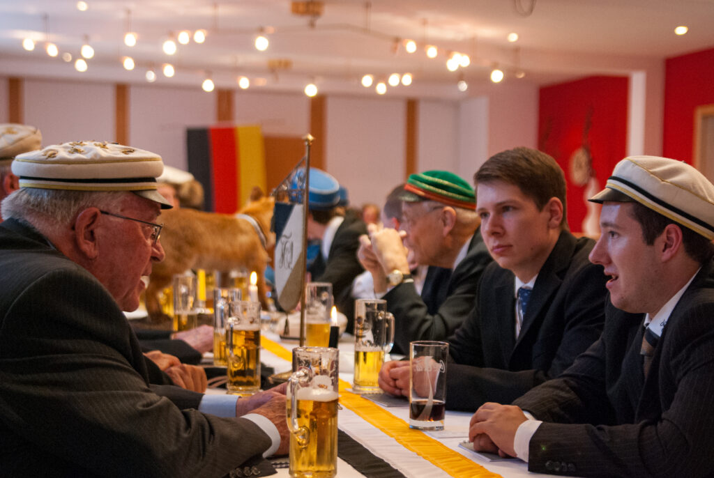 Junge und alter Personen sitzen an einem Tisch und unterhalten sich.