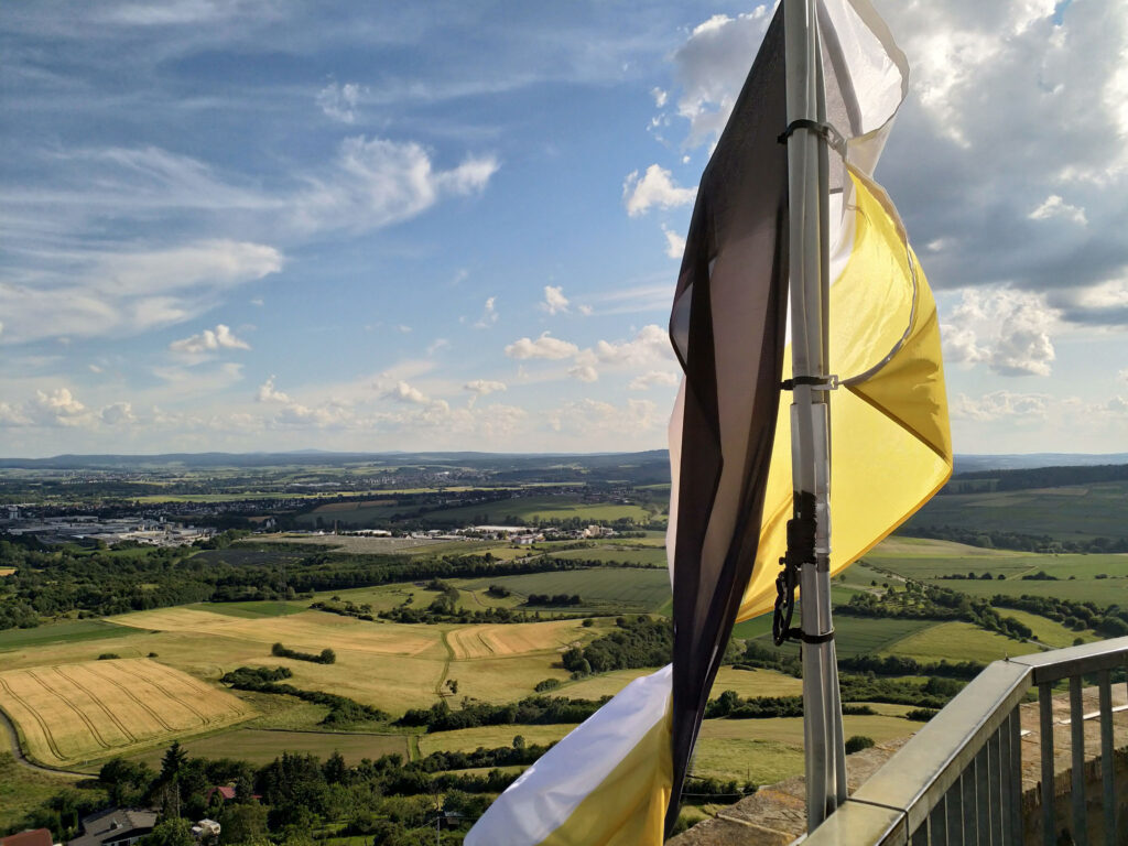 Blick auf das Gießener Land. Im Vordergrund ist eine Fahne in den Farben Schawz-Weiß-Gold.